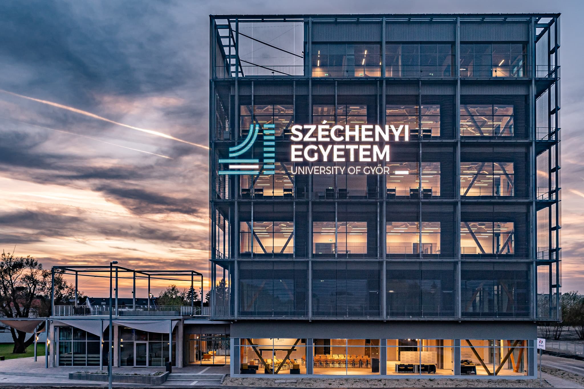 A Kocka üvegfalú épülete alkonyatkor, a Széchenyi Egyetem logójával